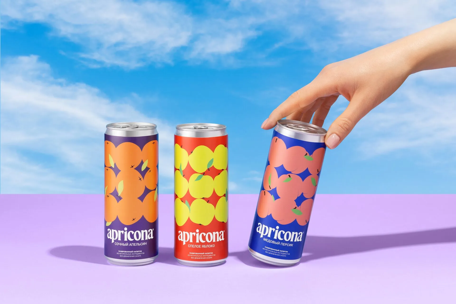Три банки Apricona на сиреневом столе, рука берёт одну